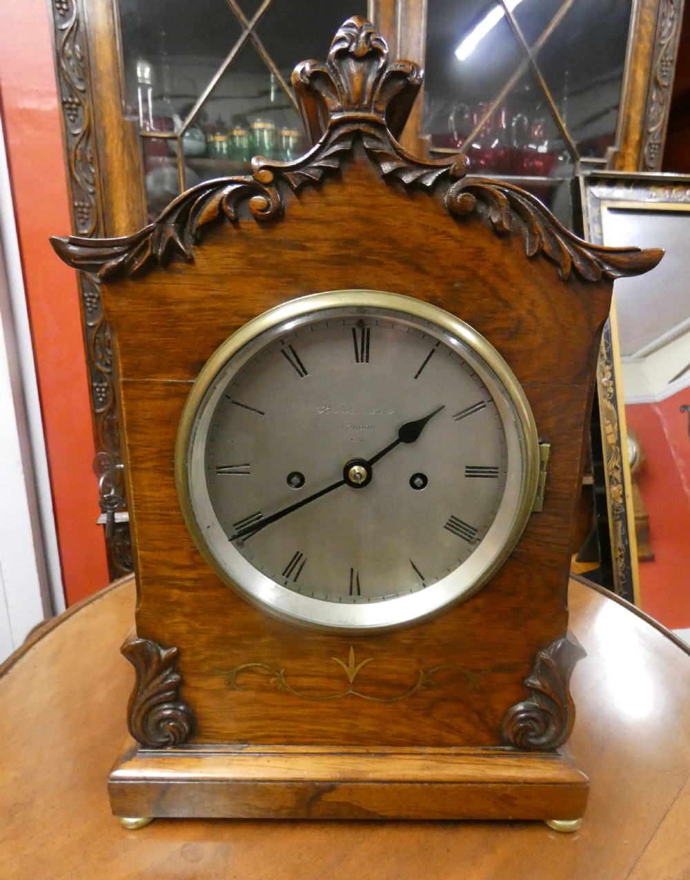 A William IV wooden bracket clock with carved foliate corner accents, brass scroll inlay, and a round dial displaying Roman numerals. View IX
