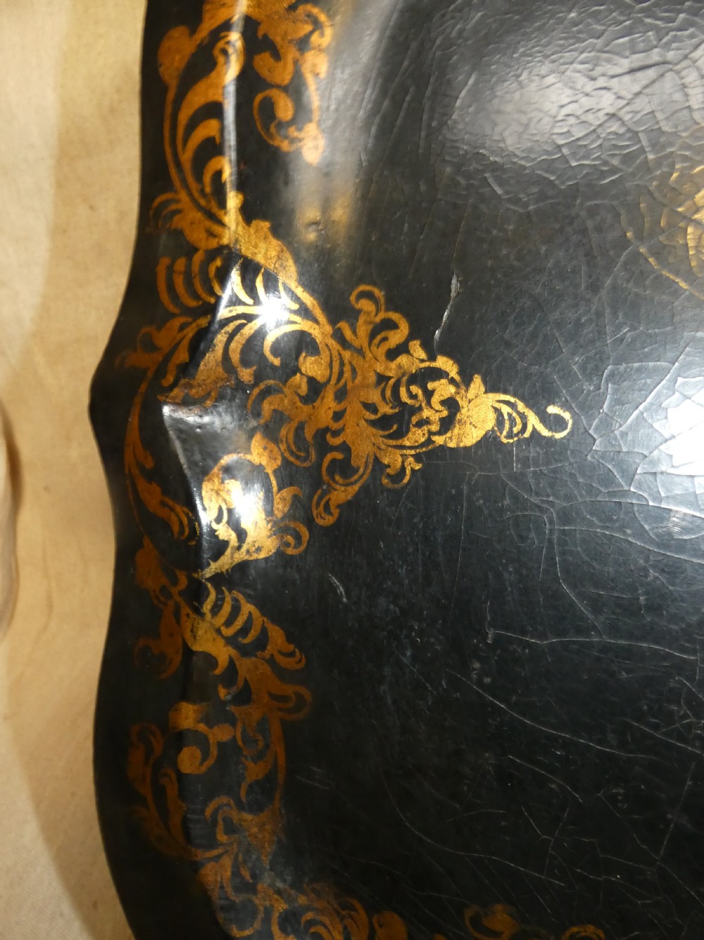 A black Victorian papier-mache serving tray featuring a scalloped rim, gilded scrollwork ornamentation, and a hand-painted floral centrepiece inlaid with mother-of-pearl. View III