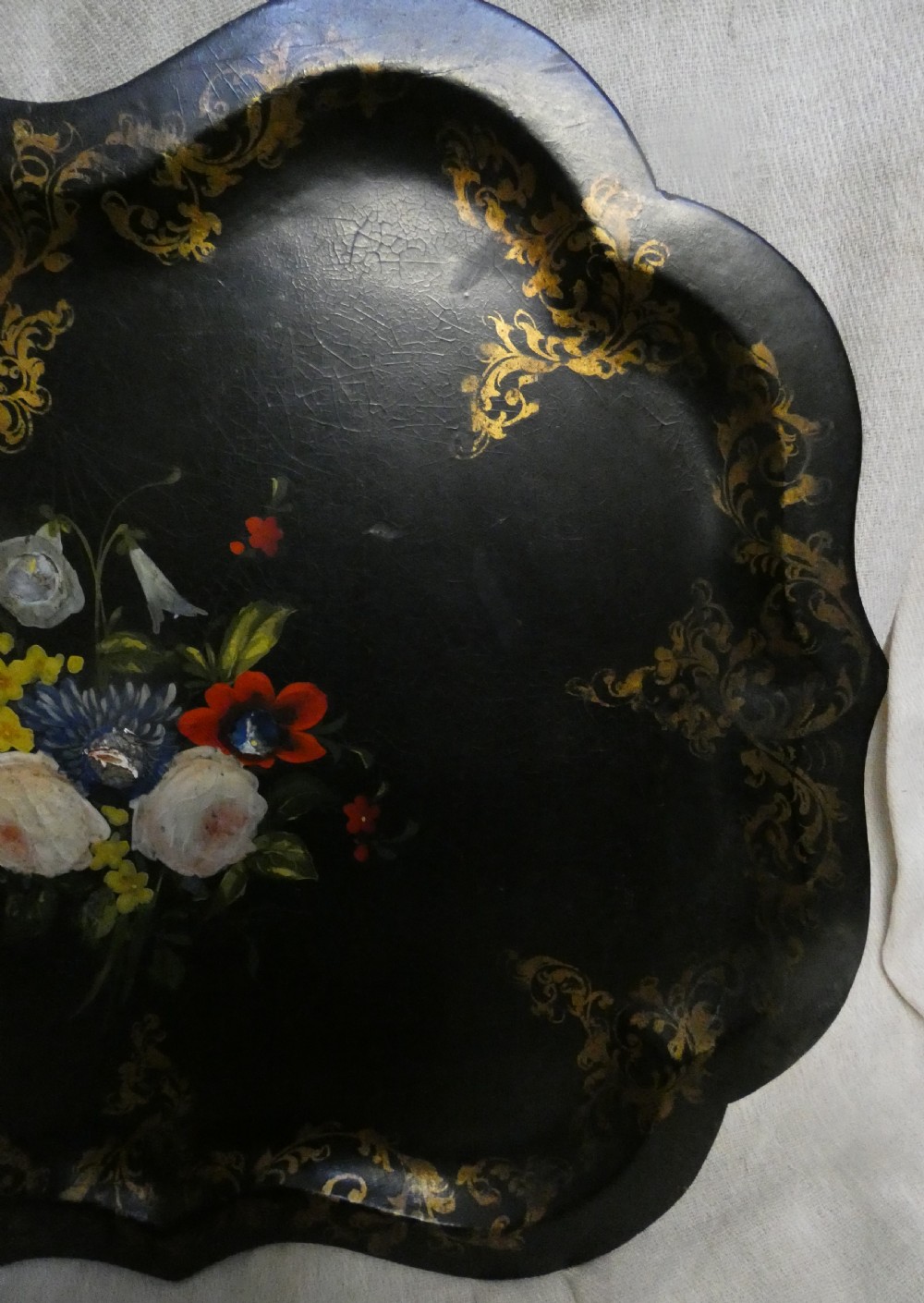 A black Victorian papier-mache serving tray featuring a scalloped rim, gilded scrollwork ornamentation, and a hand-painted floral centrepiece inlaid with mother-of-pearl. View VI
