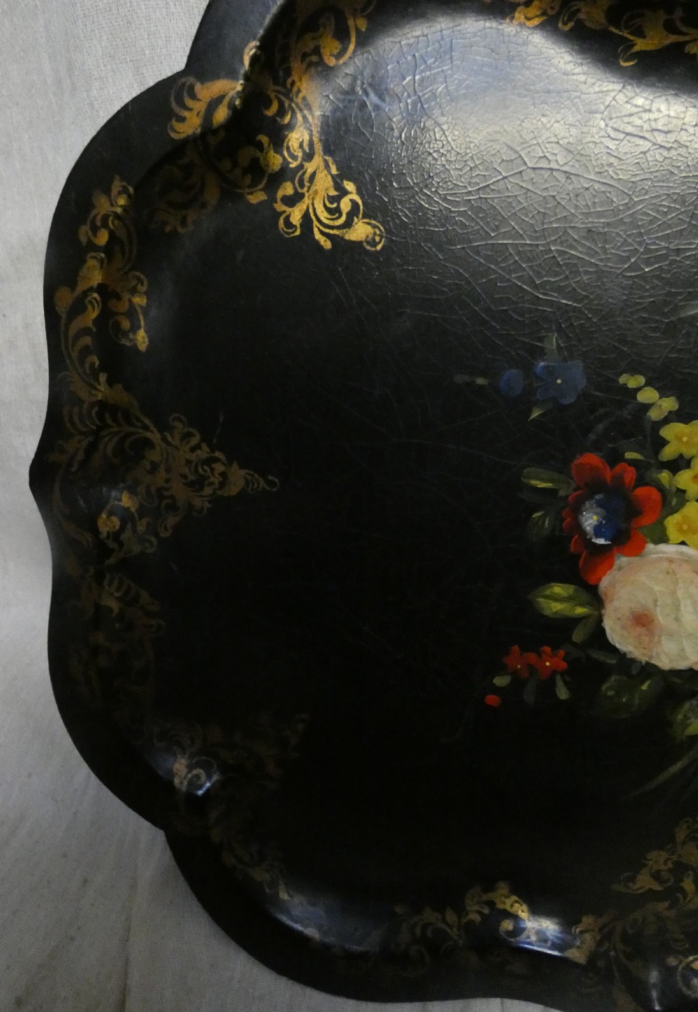 A black Victorian papier-mache serving tray featuring a scalloped rim, gilded scrollwork ornamentation, and a hand-painted floral centrepiece inlaid with mother-of-pearl. View VII