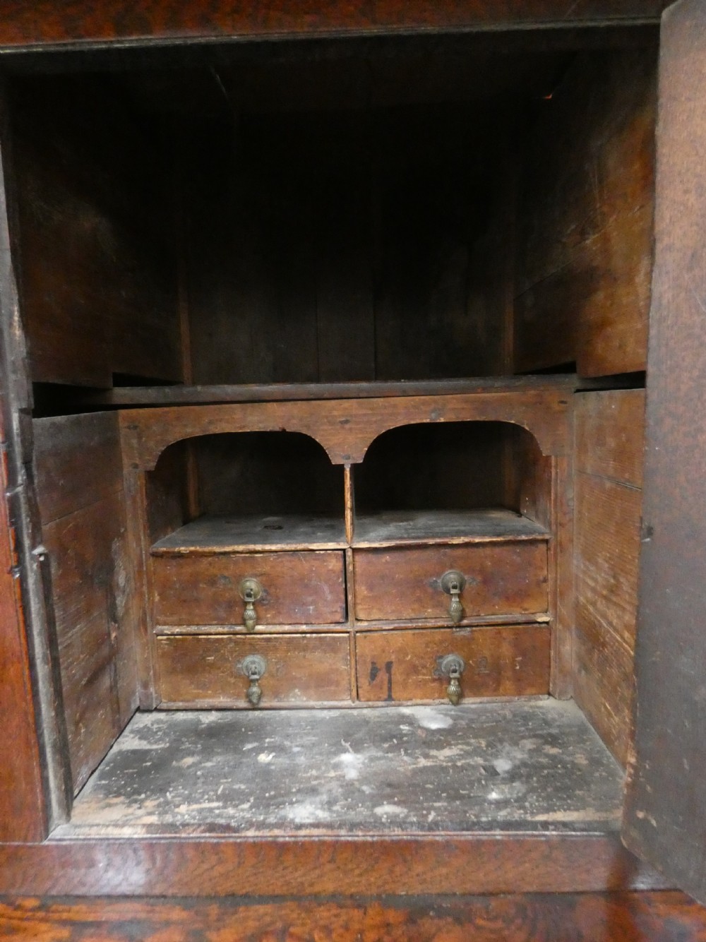 An antique dark oak Welsh deuddarn featuring a two-tiered design with arched fielded panels, brass handles, and carved drop pendants along the top canopy. View V