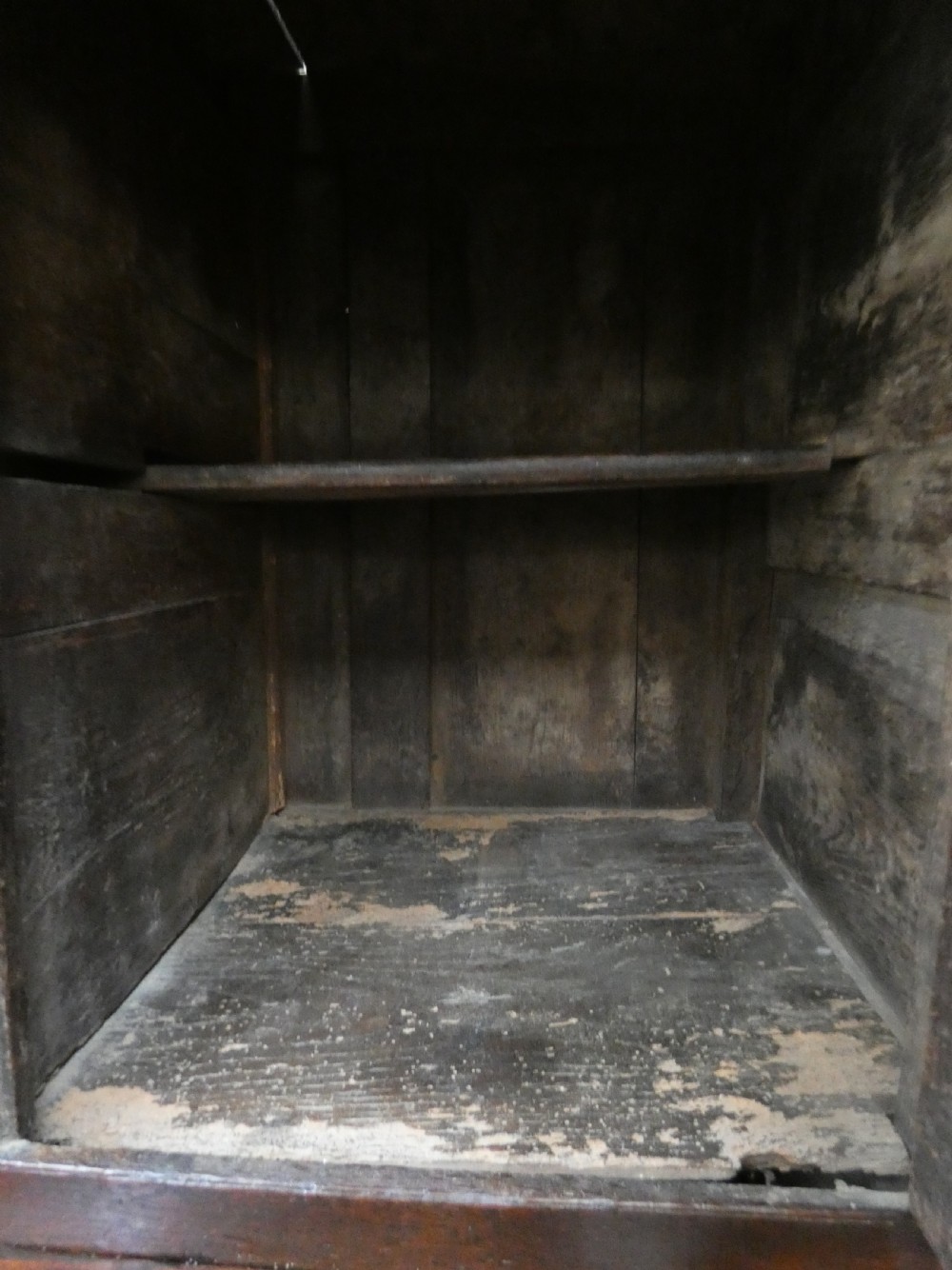 An antique dark oak Welsh deuddarn featuring a two-tiered design with arched fielded panels, brass handles, and carved drop pendants along the top canopy. View VI