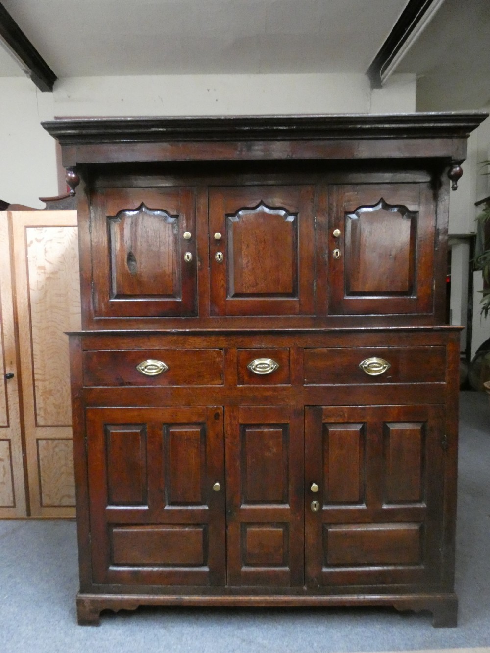 An antique dark oak Welsh deuddarn featuring a two-tiered design with arched fielded panels, brass handles, and carved drop pendants along the top canopy. View VIII