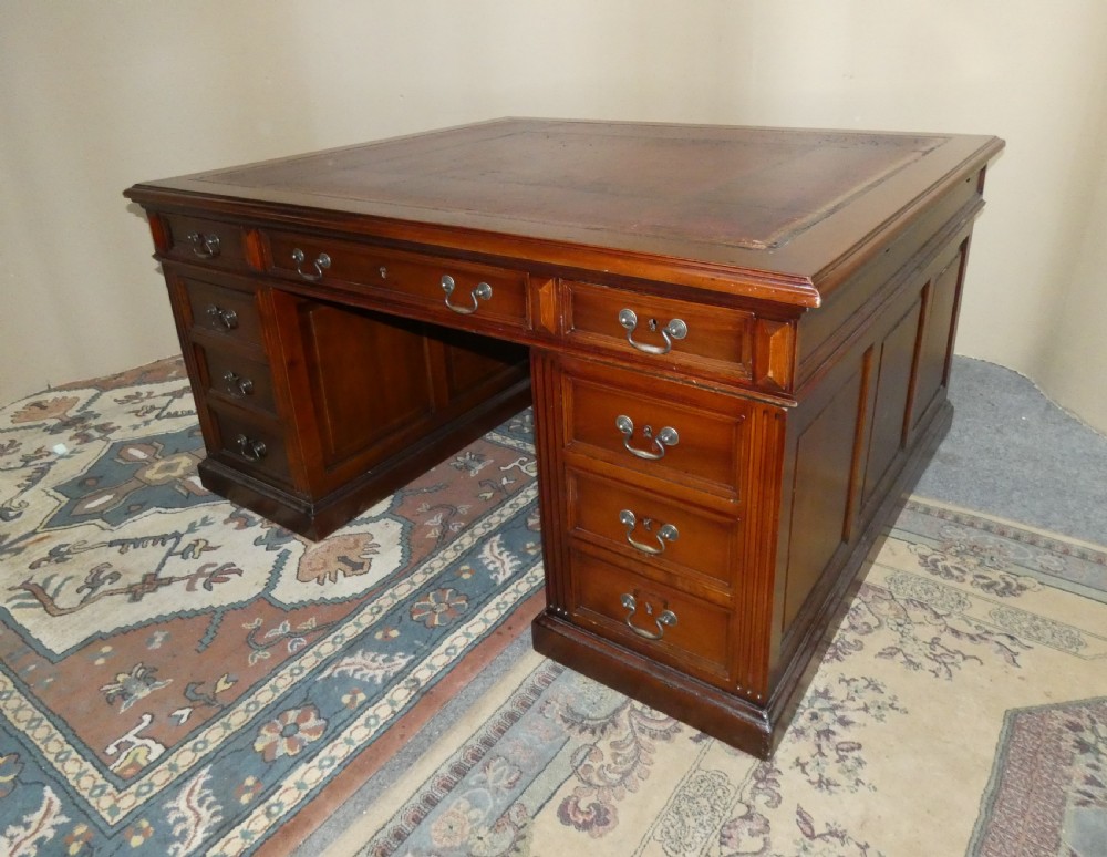 A large mahogany partners desk featuring a brown leather-inlaid top, twin pedestal drawers, and brass swan-neck handles.