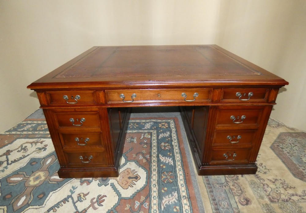 A large mahogany partners desk featuring a brown leather-inlaid top, twin pedestal drawers, and brass swan-neck handles. View II