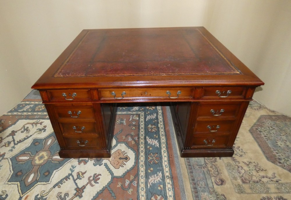 A large mahogany partners desk featuring a brown leather-inlaid top, twin pedestal drawers, and brass swan-neck handles. View III