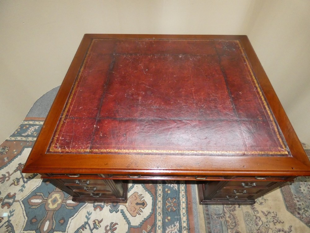 A large mahogany partners desk featuring a brown leather-inlaid top, twin pedestal drawers, and brass swan-neck handles. View V