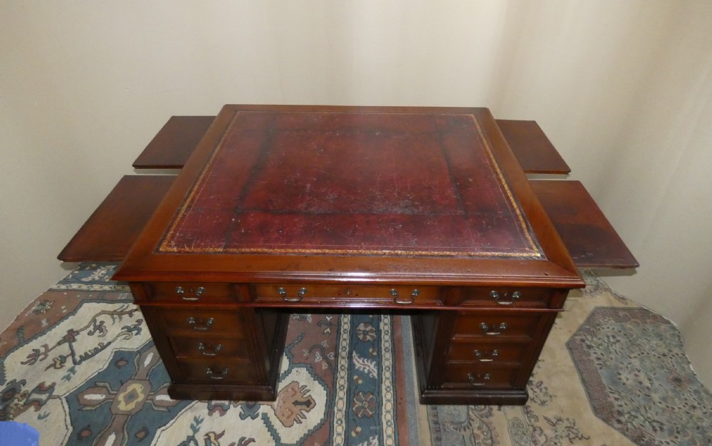 A large mahogany partners desk featuring a brown leather-inlaid top, twin pedestal drawers, and brass swan-neck handles. View VI