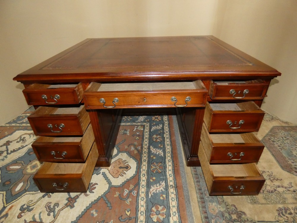 A large mahogany partners desk featuring a brown leather-inlaid top, twin pedestal drawers, and brass swan-neck handles. View VII