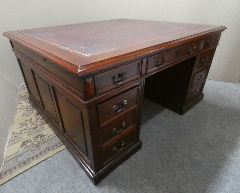 A large mahogany partners desk featuring a brown leather-inlaid top, twin pedestal drawers, and brass swan-neck handles. View X