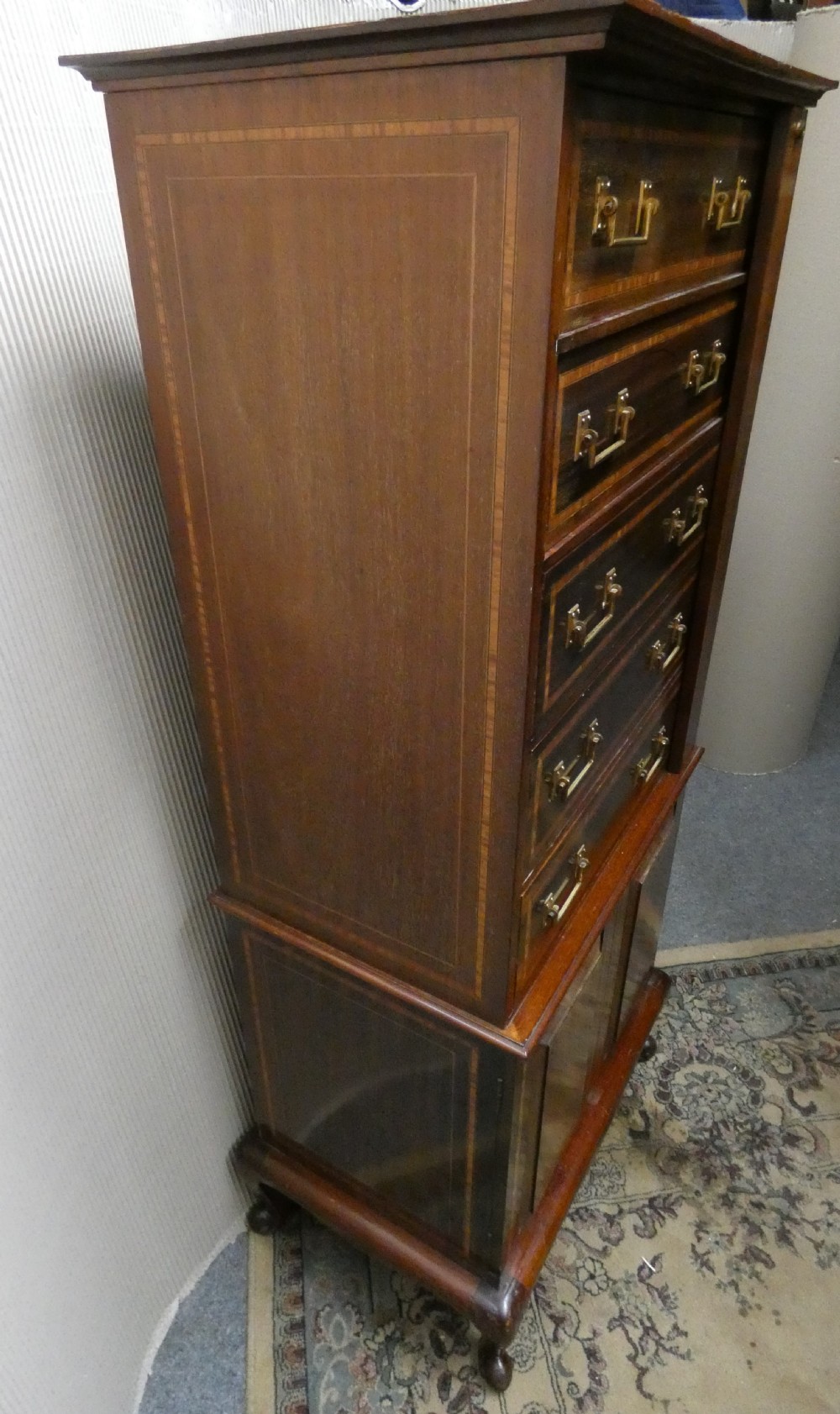 A tall antique mahogany collectors cabinet featuring five shallow upper drawers with brass handles, a hinged side locking bar, and a two-door lower cupboard resting on cabriole legs. View III