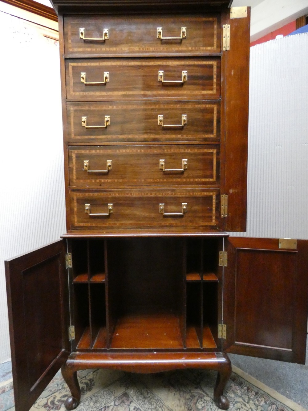 A tall antique mahogany collectors cabinet featuring five shallow upper drawers with brass handles, a hinged side locking bar, and a two-door lower cupboard resting on cabriole legs. View VI
