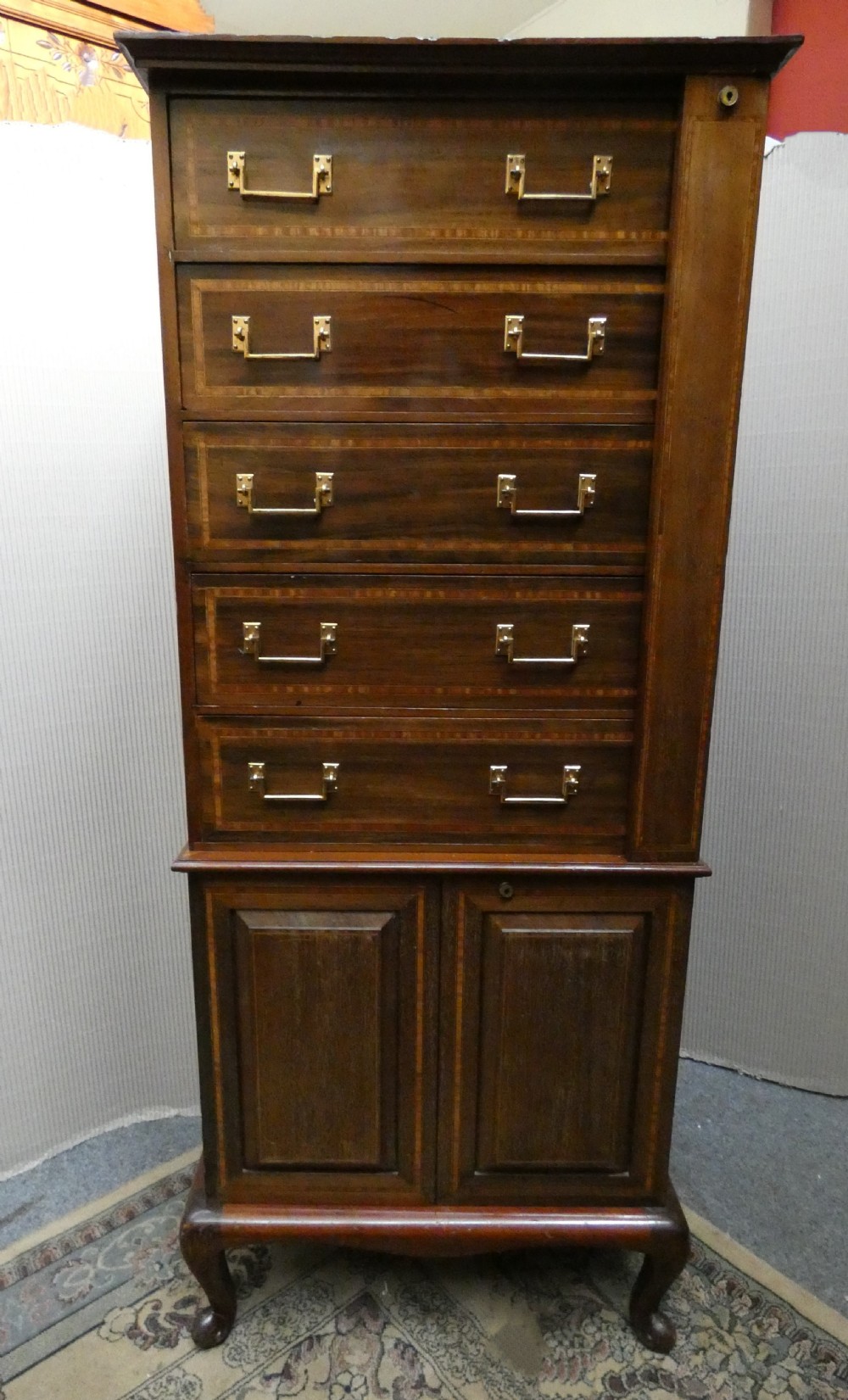 A tall antique mahogany collectors cabinet featuring five shallow upper drawers with brass handles, a hinged side locking bar, and a two-door lower cupboard resting on cabriole legs. View VII