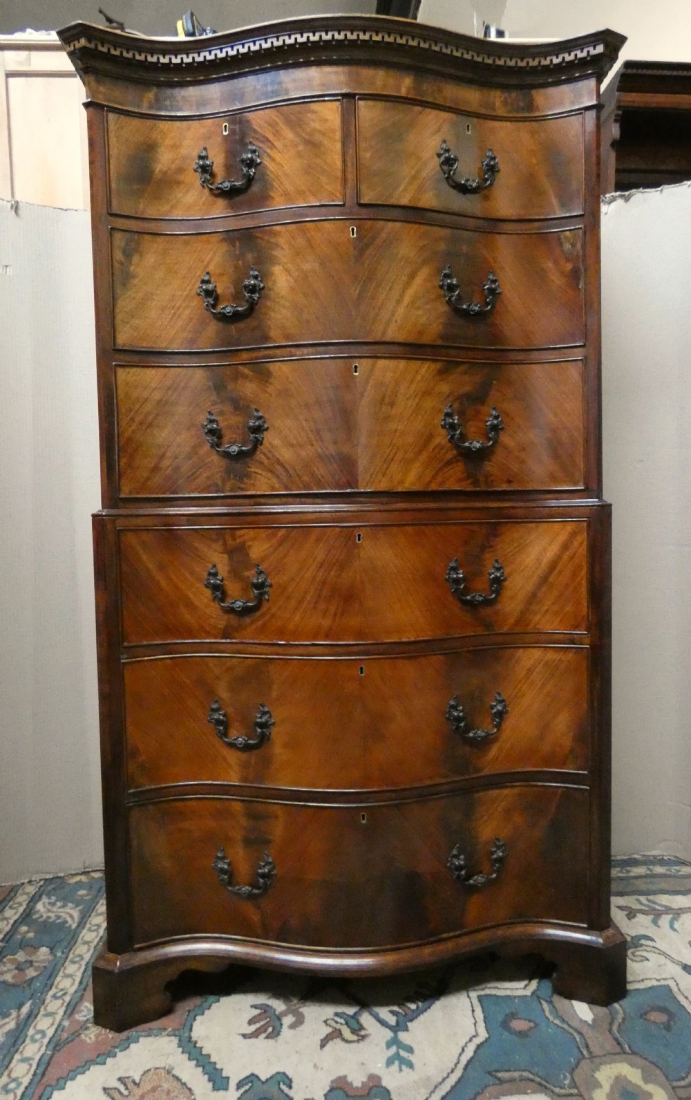 A Georgian flame mahogany chest-on-chest featuring a serpentine front, dentil moulding along the upper cornice, dark brass handles, and bracket feet.