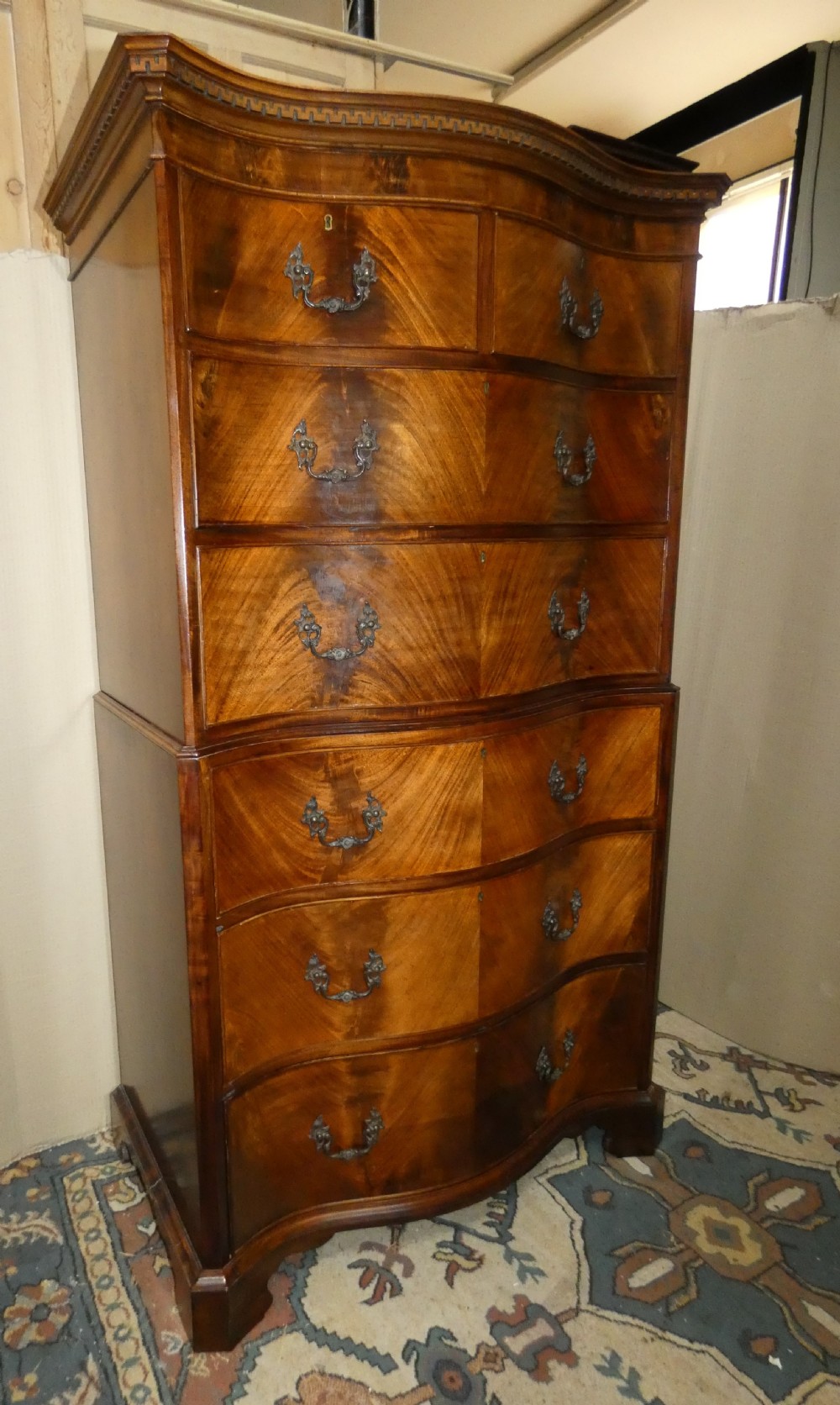 A Georgian flame mahogany chest-on-chest featuring a serpentine front, dentil moulding along the upper cornice, dark brass handles, and bracket feet. View II