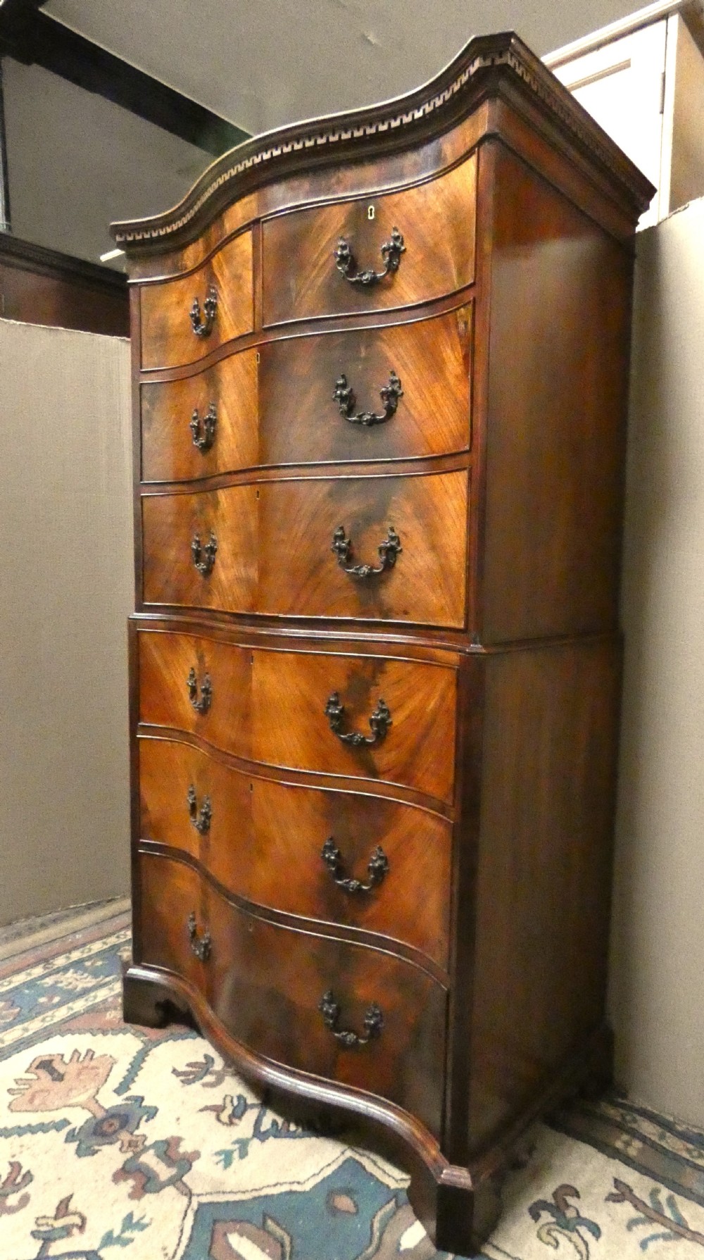 A Georgian flame mahogany chest-on-chest featuring a serpentine front, dentil moulding along the upper cornice, dark brass handles, and bracket feet. View III