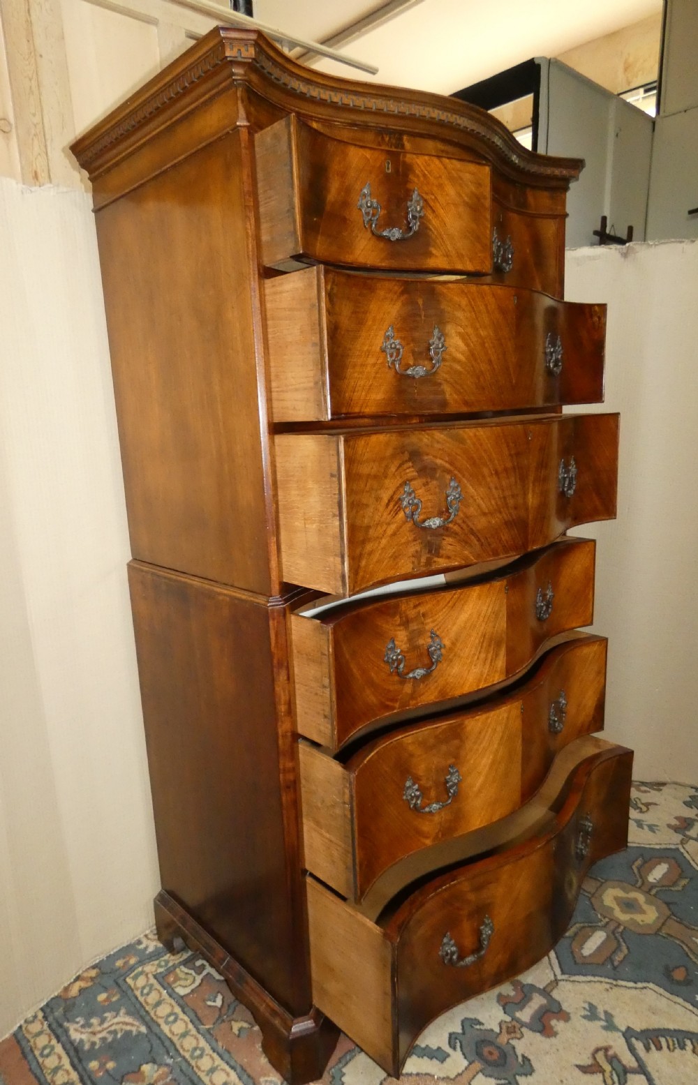 A Georgian flame mahogany chest-on-chest featuring a serpentine front, dentil moulding along the upper cornice, dark brass handles, and bracket feet. View VII