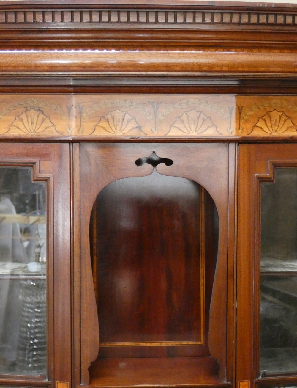 An antique mahogany display cabinet featuring inlaid satinwood decoration, carved floral door panels, glass display sections, and slender corner supports. View III