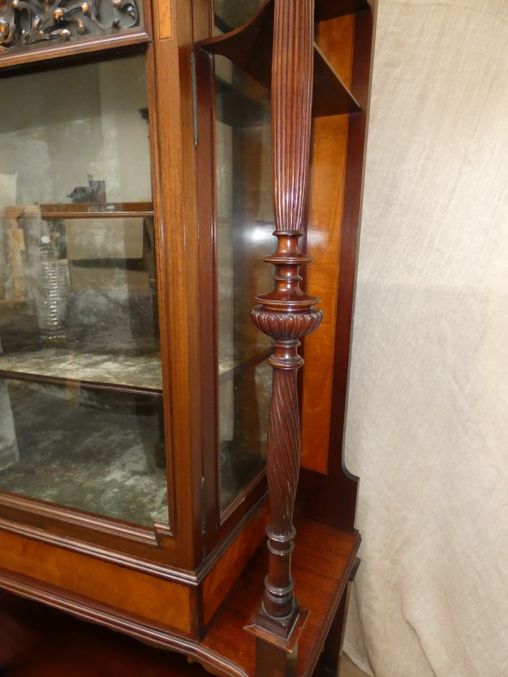An antique mahogany display cabinet featuring inlaid satinwood decoration, carved floral door panels, glass display sections, and slender corner supports. View VI