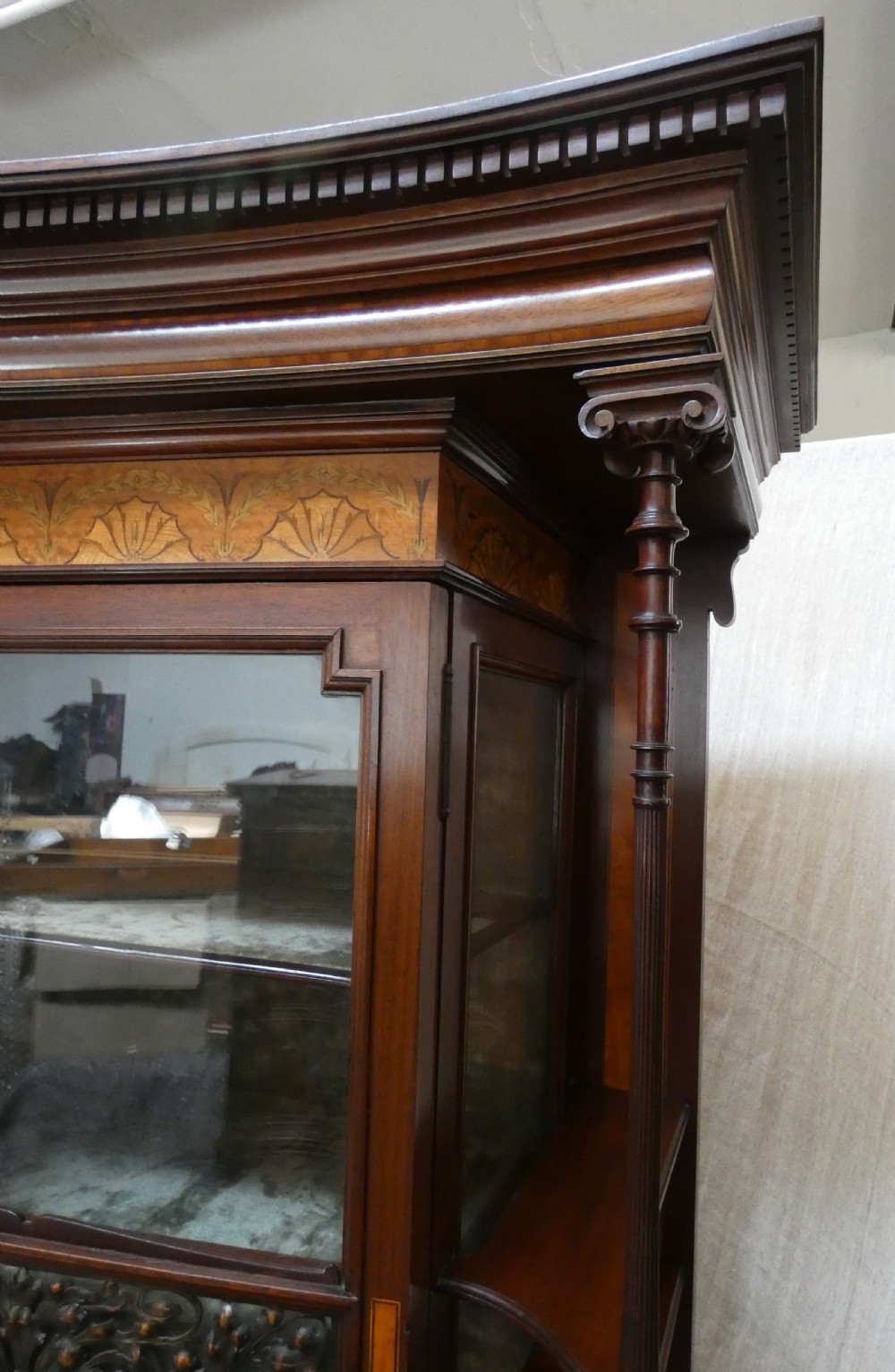 An antique mahogany display cabinet featuring inlaid satinwood decoration, carved floral door panels, glass display sections, and slender corner supports. View VII