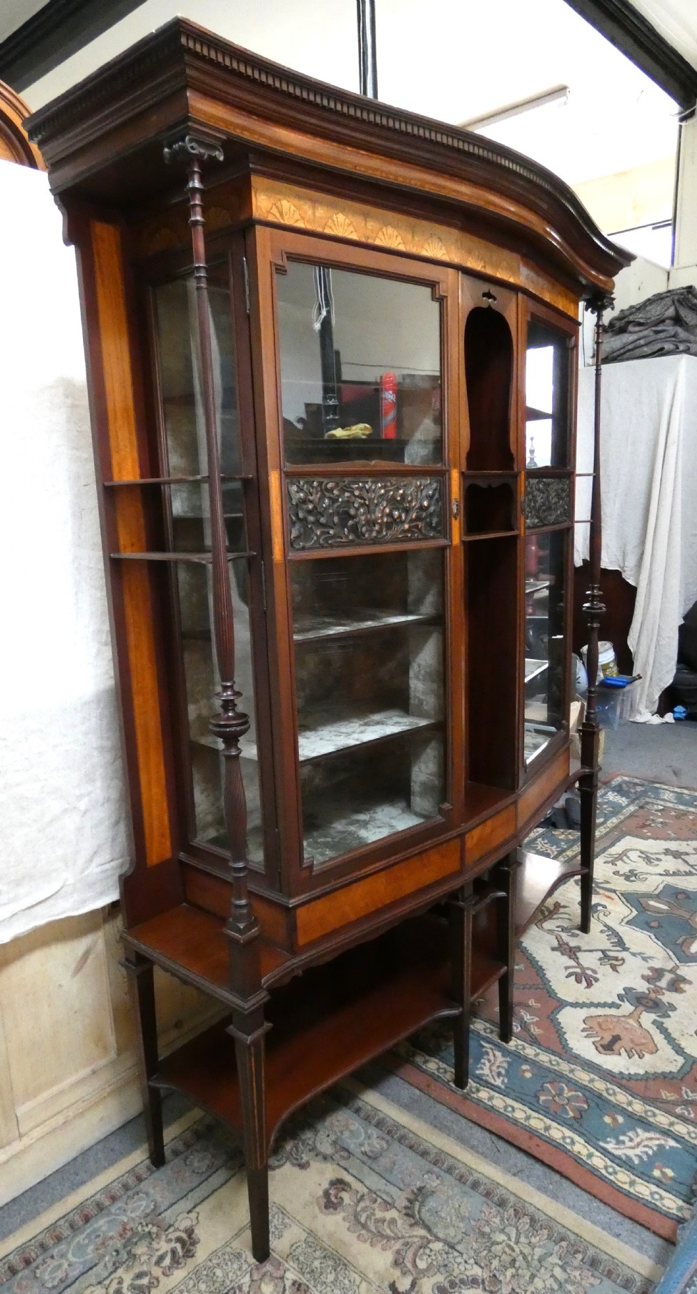 An antique mahogany display cabinet featuring inlaid satinwood decoration, carved floral door panels, glass display sections, and slender corner supports. View VIII