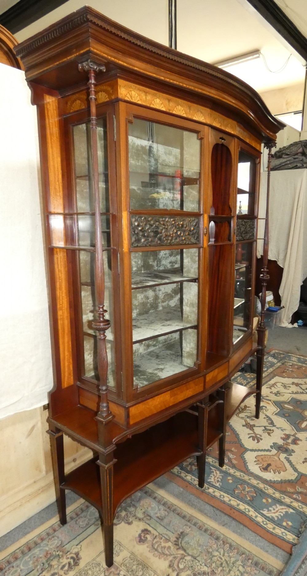An antique mahogany display cabinet featuring inlaid satinwood decoration, carved floral door panels, glass display sections, and slender corner supports. View IX