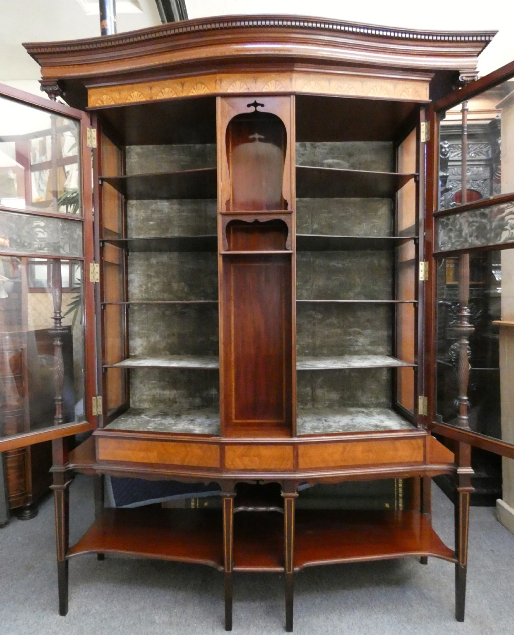 An antique mahogany display cabinet featuring inlaid satinwood decoration, carved floral door panels, glass display sections, and slender corner supports. View XII