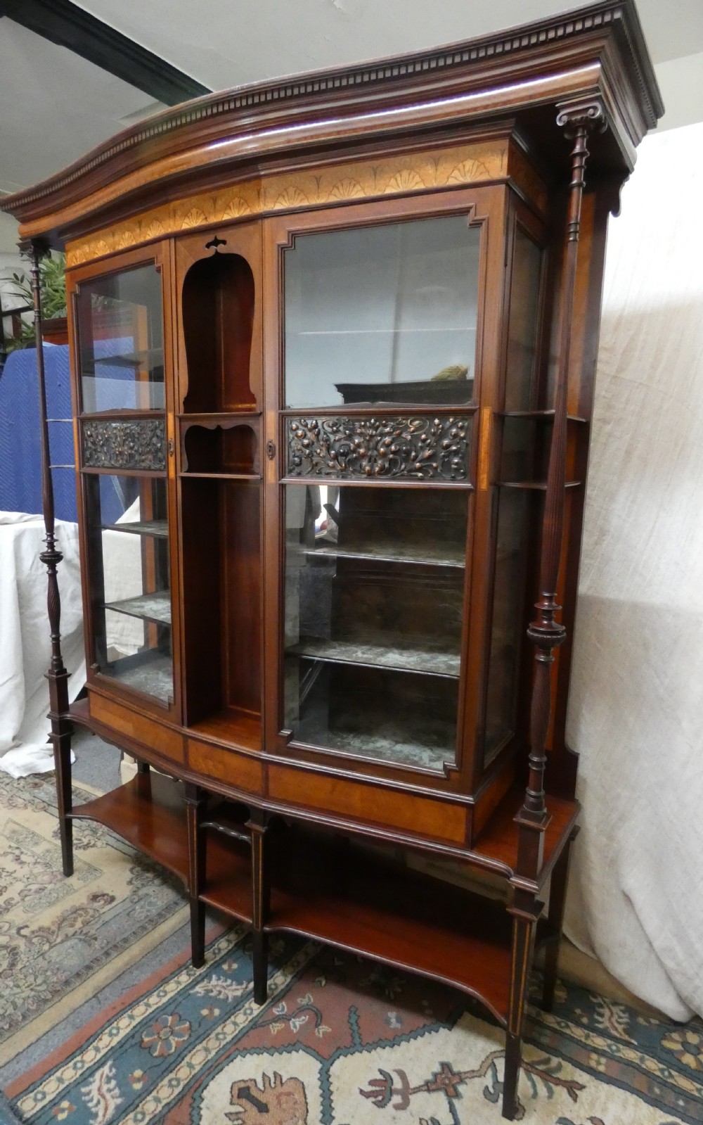 An antique mahogany display cabinet featuring inlaid satinwood decoration, carved floral door panels, glass display sections, and slender corner supports. View XIII