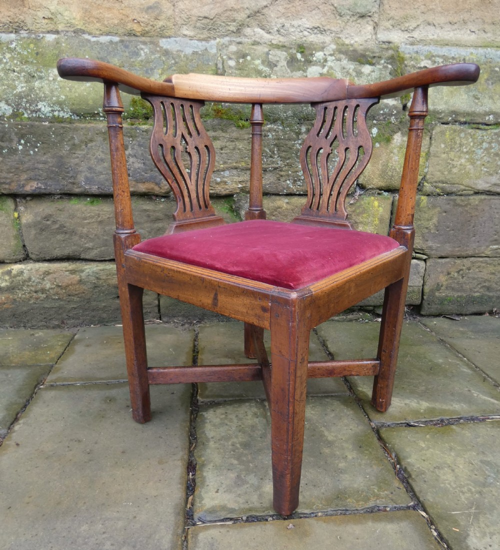 An antique Georgian mahogany corner chair featuring a curved horseshoe armrest, two pierced vase-shaped splats, turned uprights, and a red velvet upholstered seat.