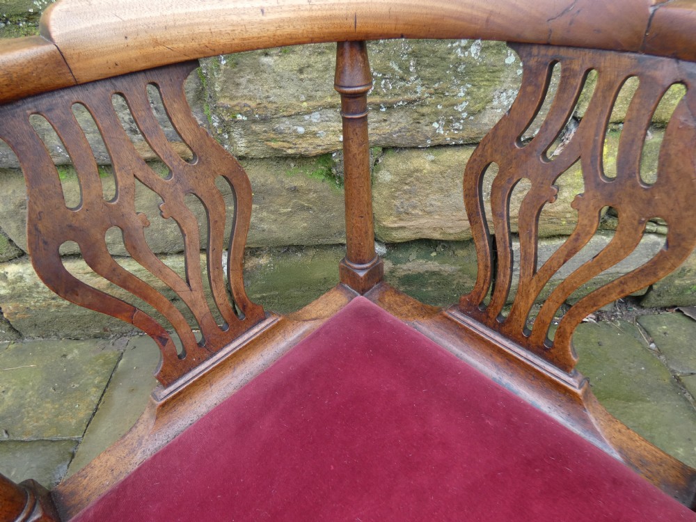 An antique Georgian mahogany corner chair featuring a curved horseshoe armrest, two pierced vase-shaped splats, turned uprights, and a red velvet upholstered seat. View III