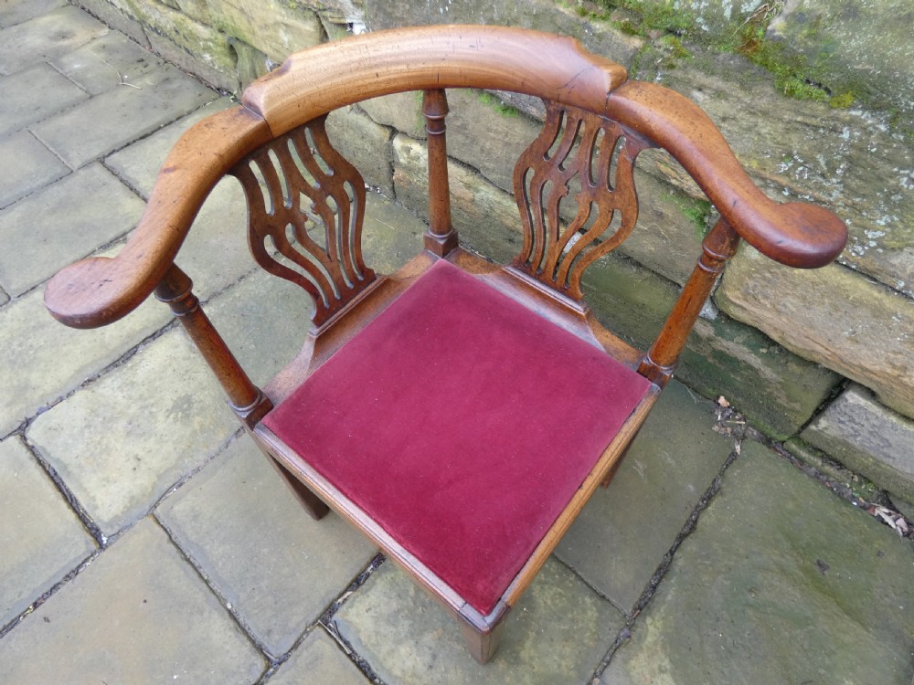 An antique Georgian mahogany corner chair featuring a curved horseshoe armrest, two pierced vase-shaped splats, turned uprights, and a red velvet upholstered seat. View VI