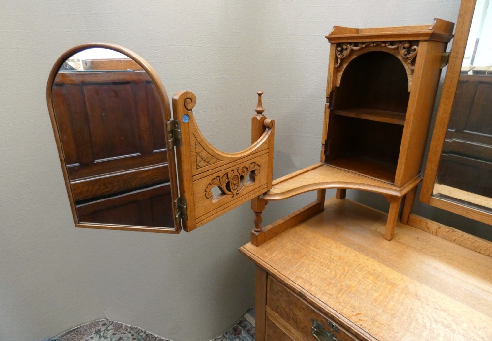 An Edwardian oak bedroom suite featuring a large three-door wardrobe with a central mirrored panel alongside a matching carved dressing table. View XV