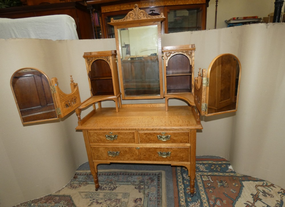 An Edwardian oak bedroom suite featuring a large three-door wardrobe with a central mirrored panel alongside a matching carved dressing table. View XVI