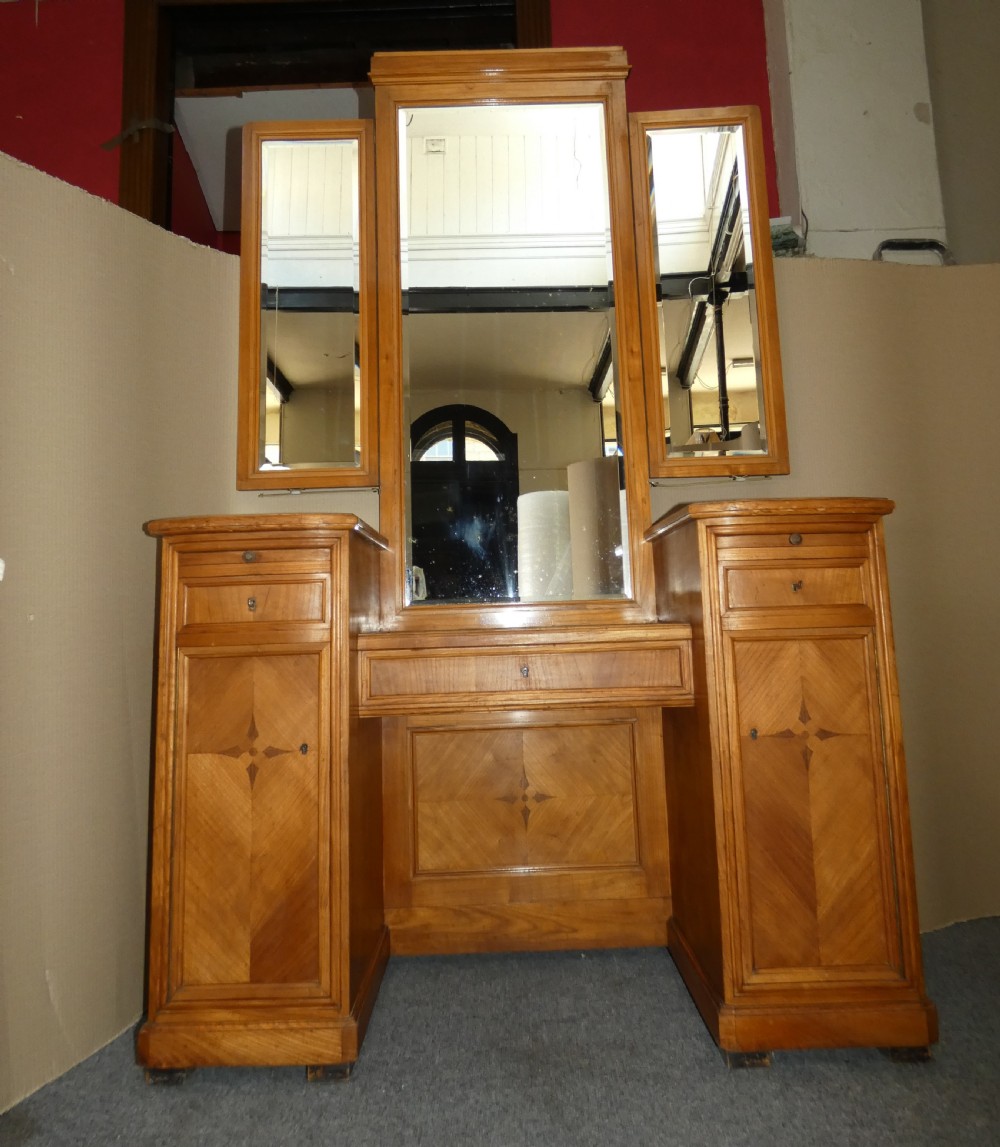A satinwood dressing table featuring a central tall mirror flanked by two adjustable wing mirrors, twin pedestal cupboards with geometric star motif parquetry, and a central drawer.