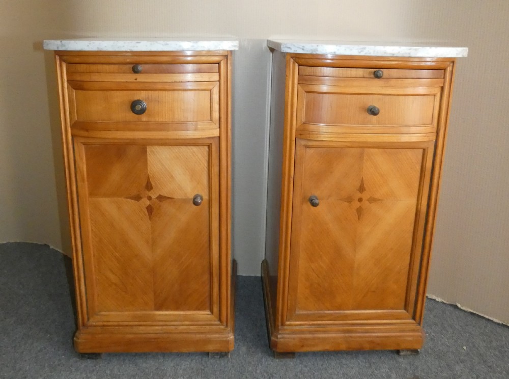 A pair of satinwood bedside cabinets with white marble tops, single drawers, pull-out slides, and marquetry inlaid cupboard doors.