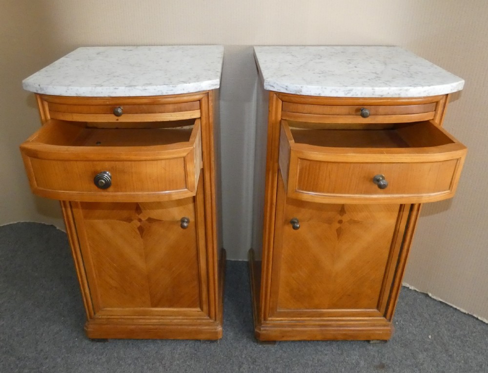 A pair of satinwood bedside cabinets with white marble tops, single drawers, pull-out slides, and marquetry inlaid cupboard doors. View V