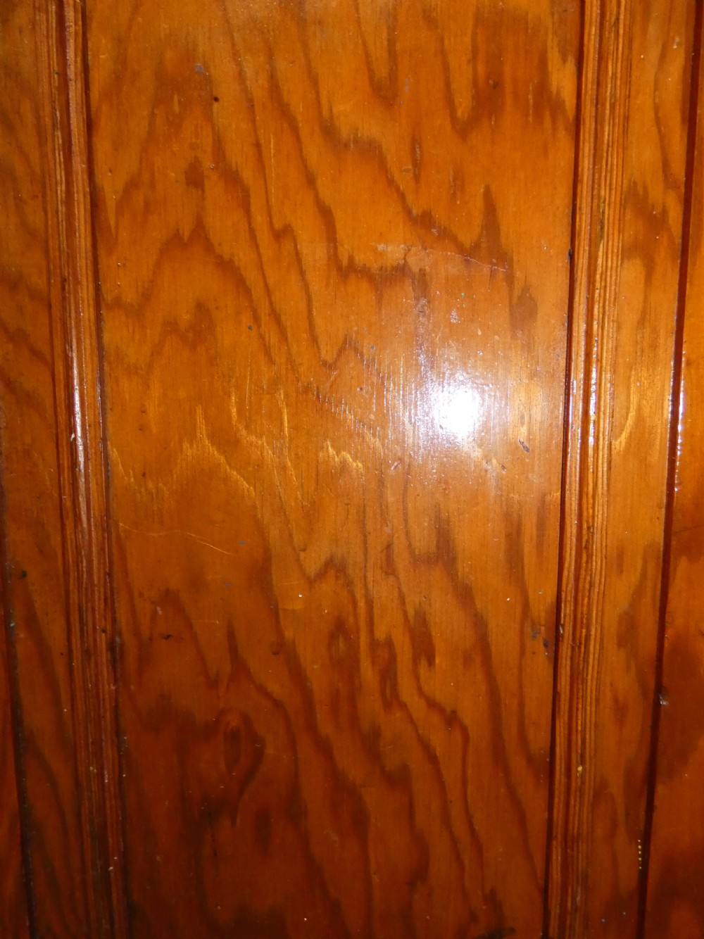 A long, low antique pitch pine cupboard featuring eight panelled doors with central keyhole escutcheons resting on a solid plinth base. View V