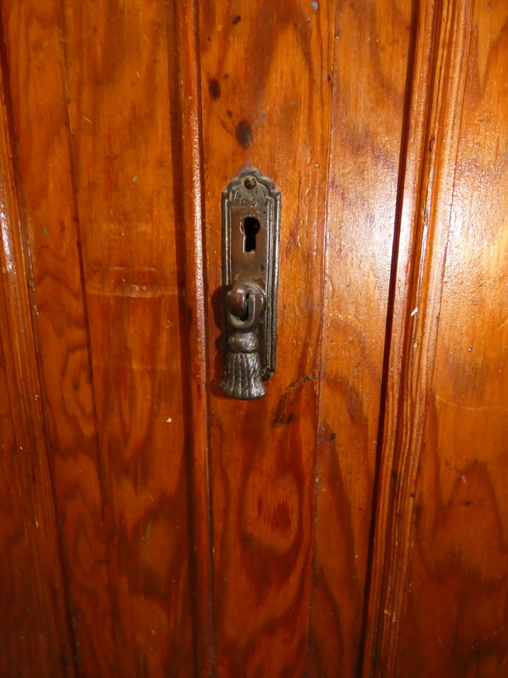 A long, low antique pitch pine cupboard featuring eight panelled doors with central keyhole escutcheons resting on a solid plinth base. View VI