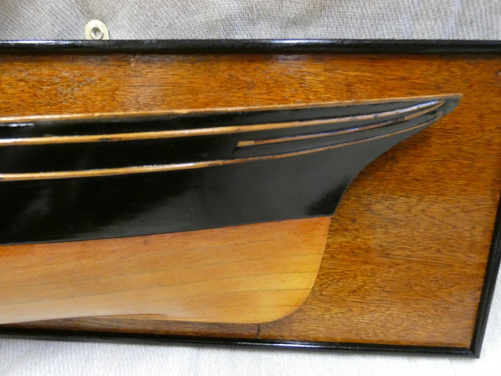 A carved wooden half-hull boat model with painted black accents, mounted on a dark wooden plaque. View II