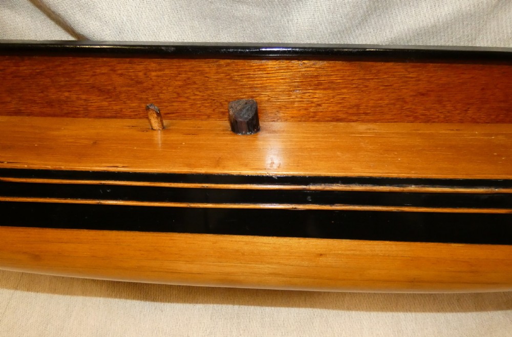 A carved wooden half-hull boat model with painted black accents, mounted on a dark wooden plaque. View III