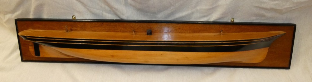 A carved wooden half-hull boat model with painted black accents, mounted on a dark wooden plaque. View V