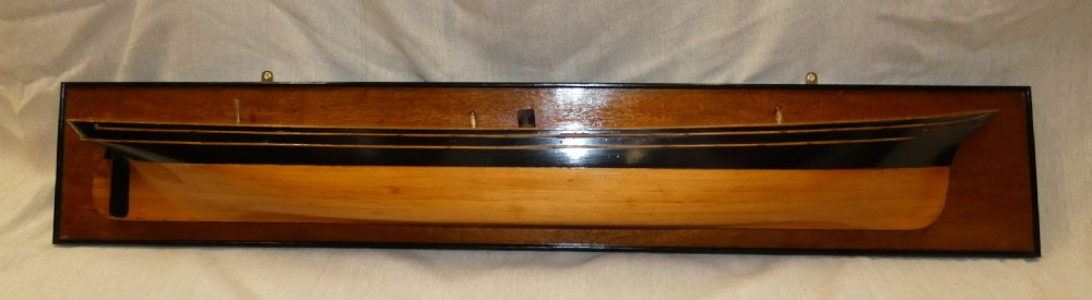 A carved wooden half-hull boat model with painted black accents, mounted on a dark wooden plaque. View VIII