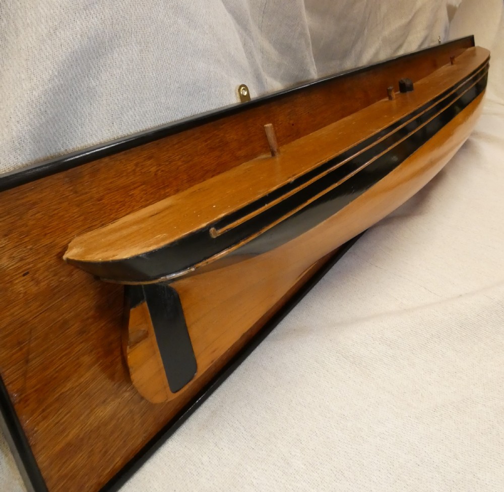 A carved wooden half-hull boat model with painted black accents, mounted on a dark wooden plaque. View IX