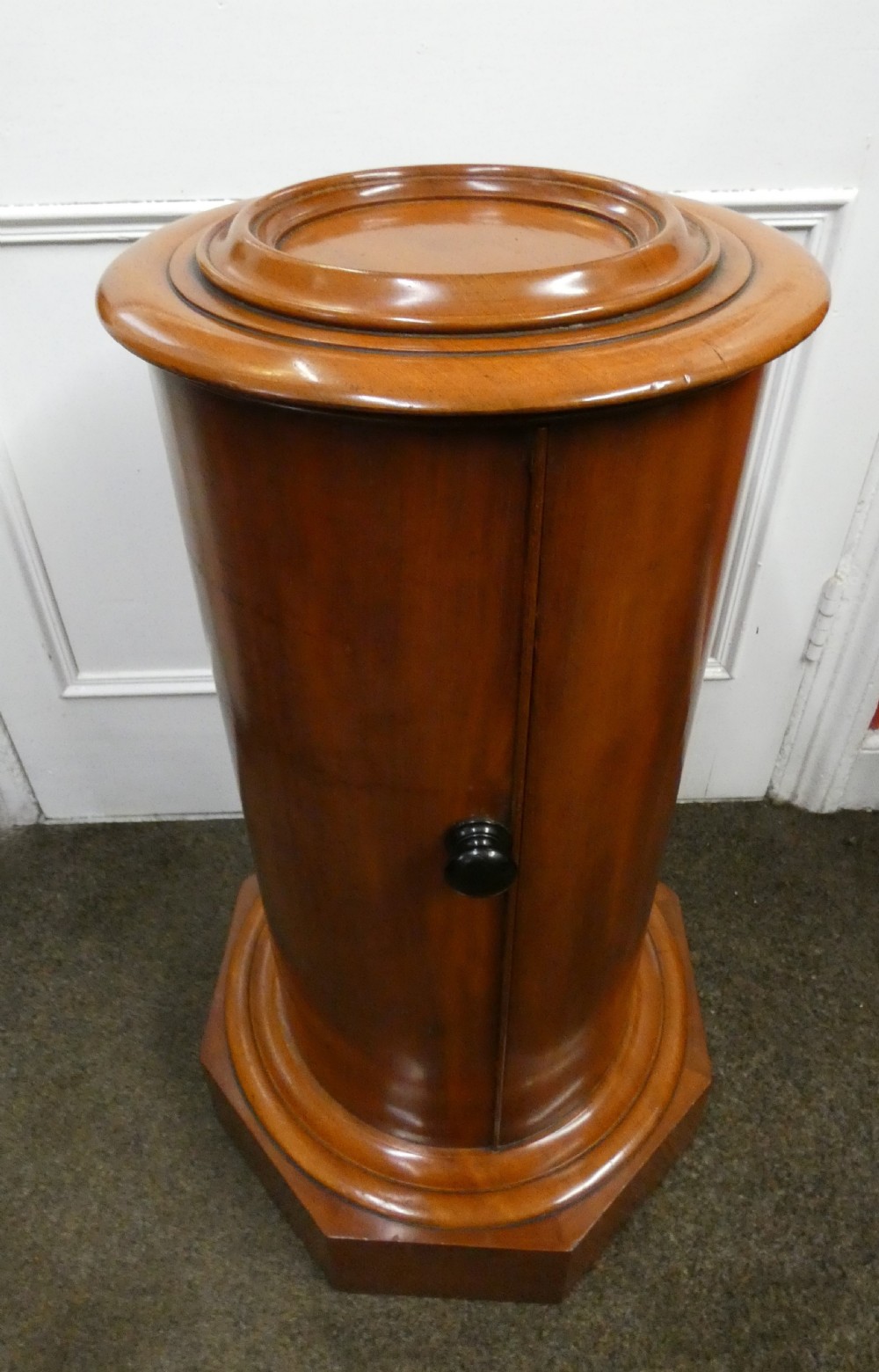 A cylindrical mahogany pot cupboard featuring a stepped circular top, a single curved door with a turned wooden knob, and an octagonal base.