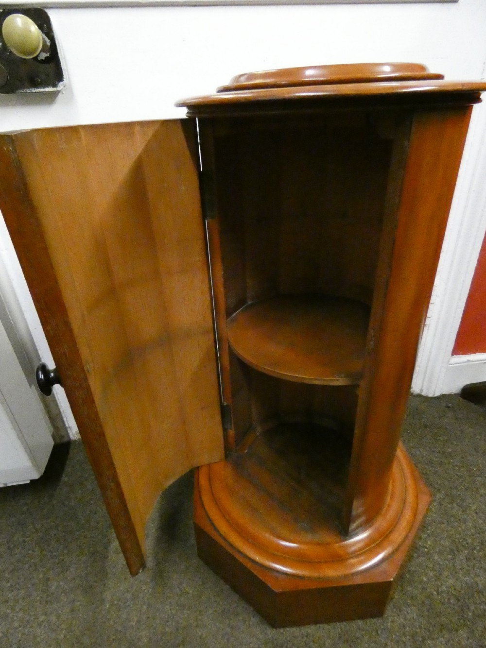 A cylindrical mahogany pot cupboard featuring a stepped circular top, a single curved door with a turned wooden knob, and an octagonal base. View III
