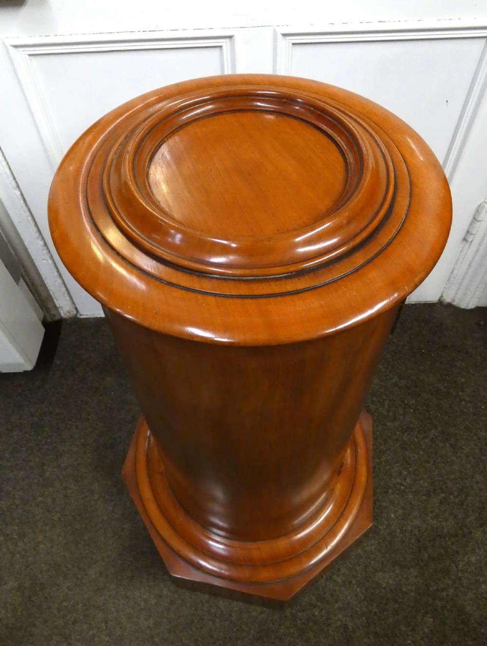 A cylindrical mahogany pot cupboard featuring a stepped circular top, a single curved door with a turned wooden knob, and an octagonal base. View VII