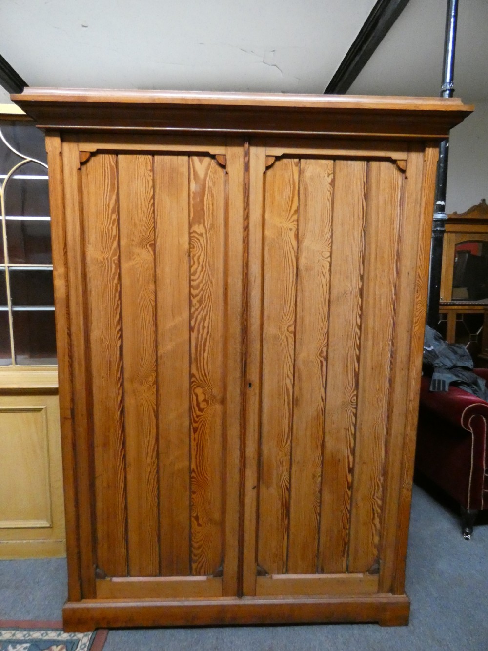 A tall Victorian pine housekeepers cupboard featuring two vertical plank-panelled doors, a projected moulded top cornice, and a sturdy plinth base.