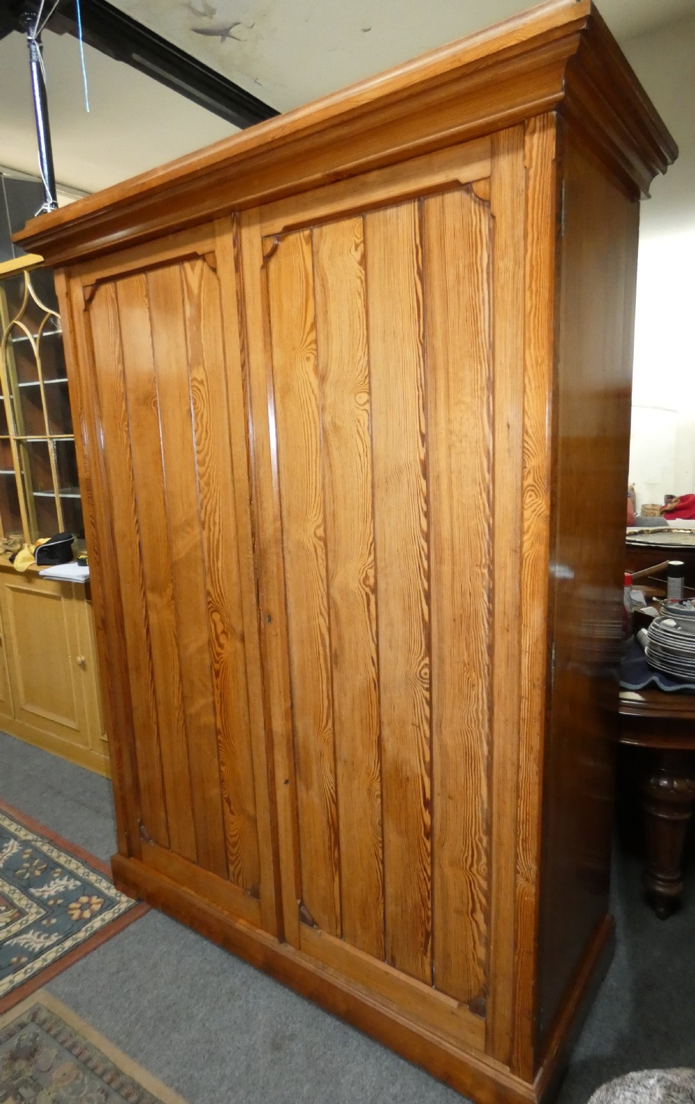 A tall Victorian pine housekeepers cupboard featuring two vertical plank-panelled doors, a projected moulded top cornice, and a sturdy plinth base. View II