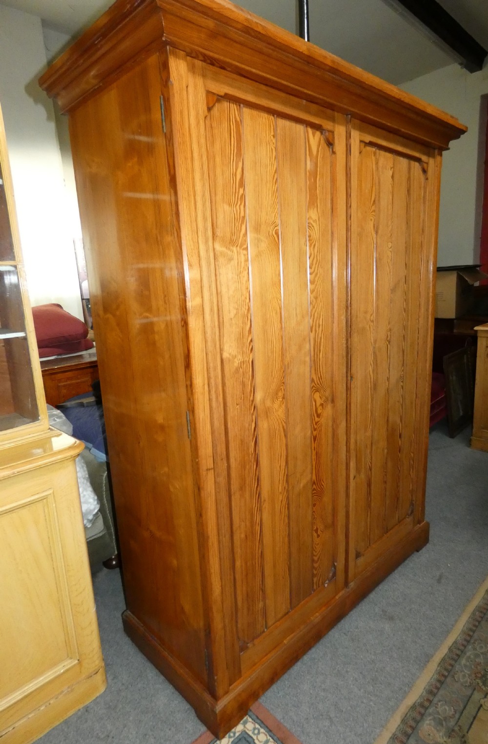 A tall Victorian pine housekeepers cupboard featuring two vertical plank-panelled doors, a projected moulded top cornice, and a sturdy plinth base. View III