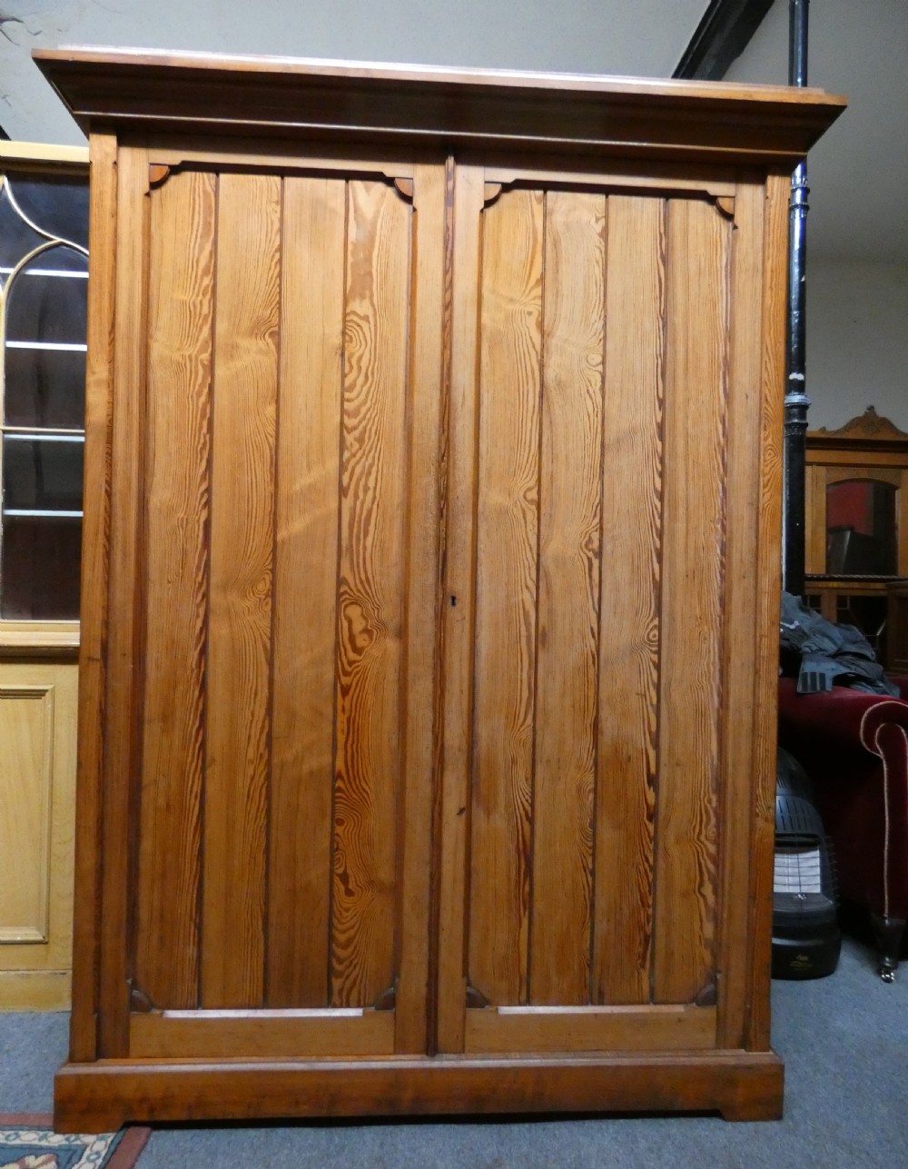 A tall Victorian pine housekeepers cupboard featuring two vertical plank-panelled doors, a projected moulded top cornice, and a sturdy plinth base. View IV